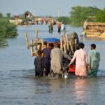 Men walk along a flooded road with their belongings, following rains and floods during the monsoon season in Suhbatpur